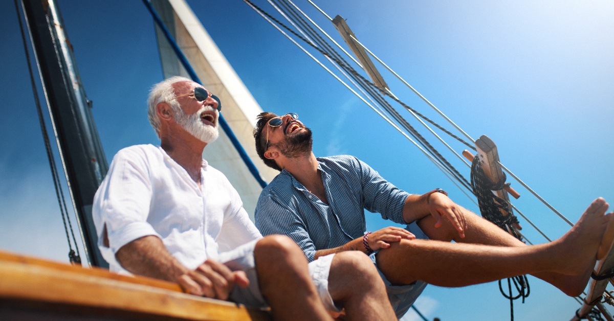 Ein älterer und ein jüngerer Herr sitzen vorne auf einem Segelboot und schauen himmelwärts.